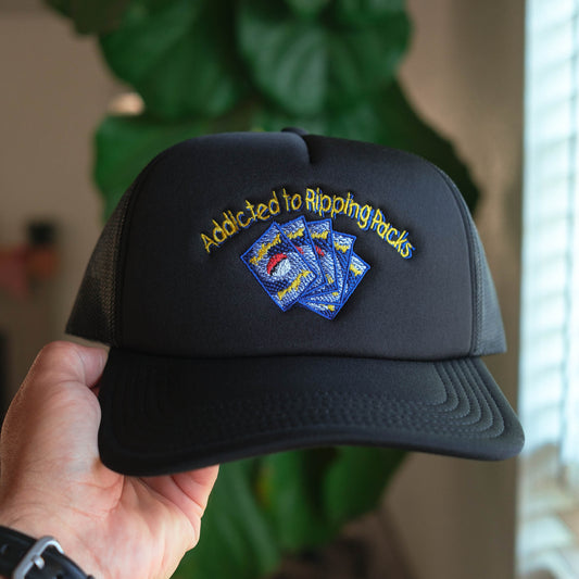 Black cap with embroidered text and cards held by a hand, blurred indoor background