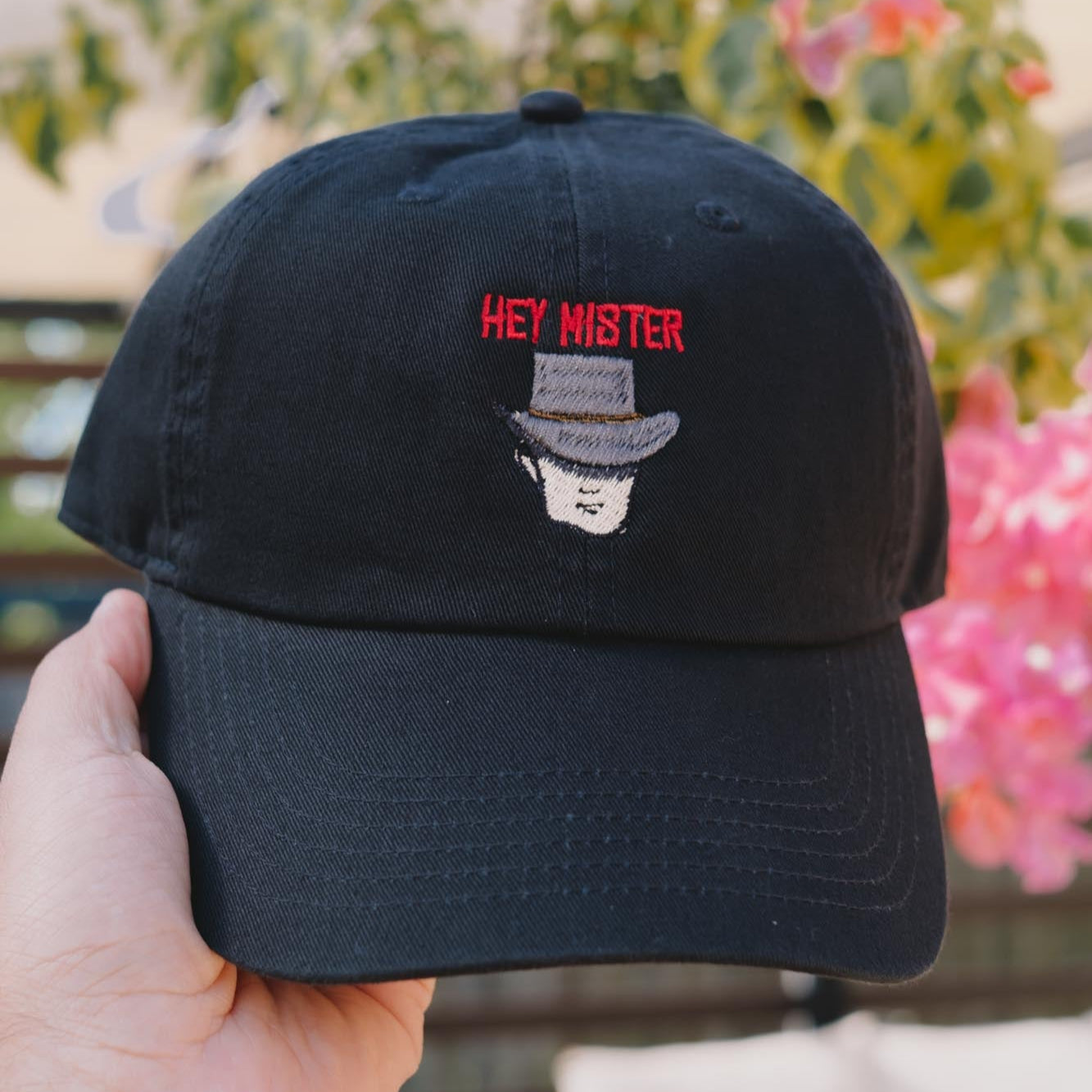A black embroidered dad hat with 'HEY MISTER' text and a cowboy hat illustration on the front.