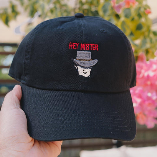 A black embroidered dad hat with 'HEY MISTER' text and a cowboy hat illustration on the front.