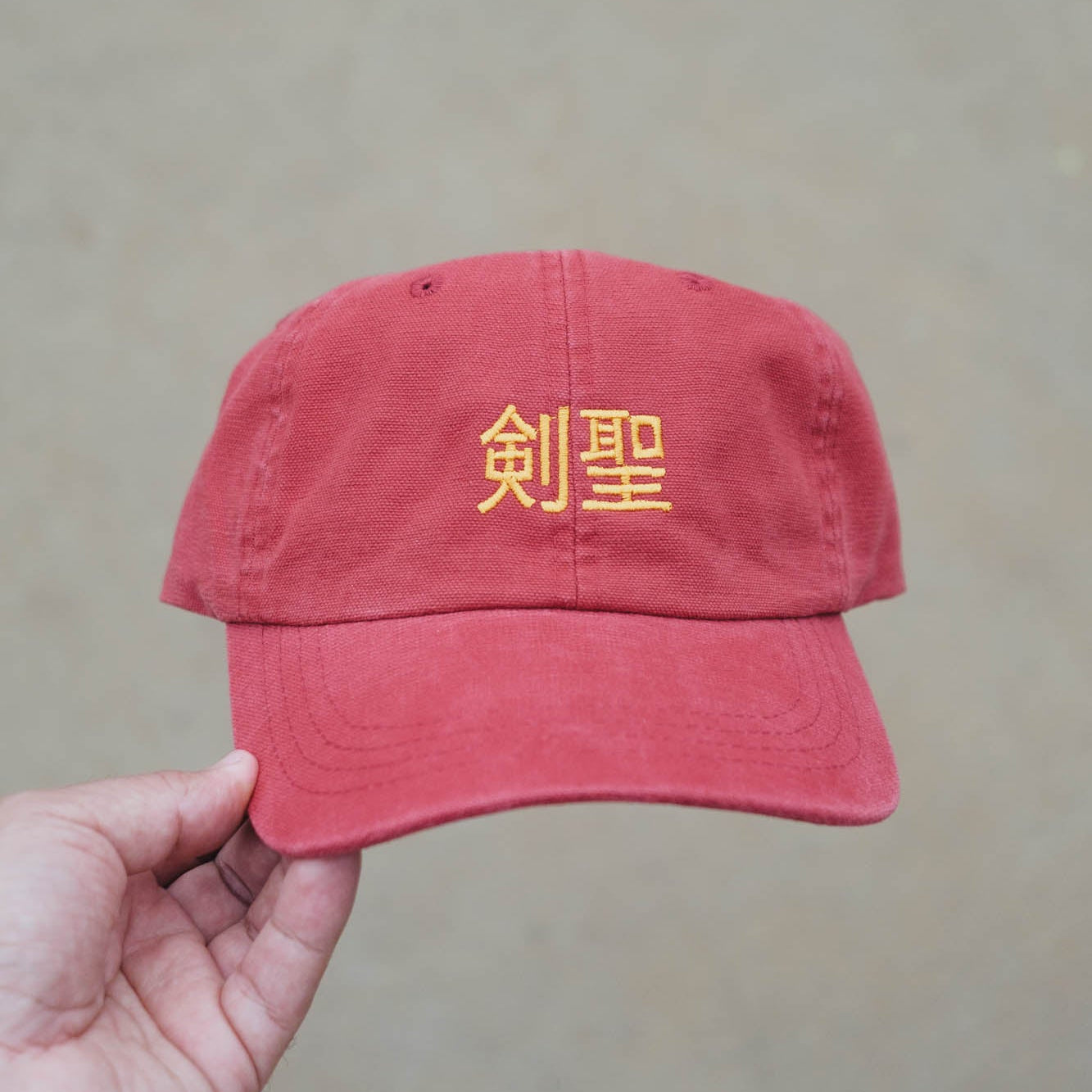 Red cap with yellow text held by a hand against a beige background