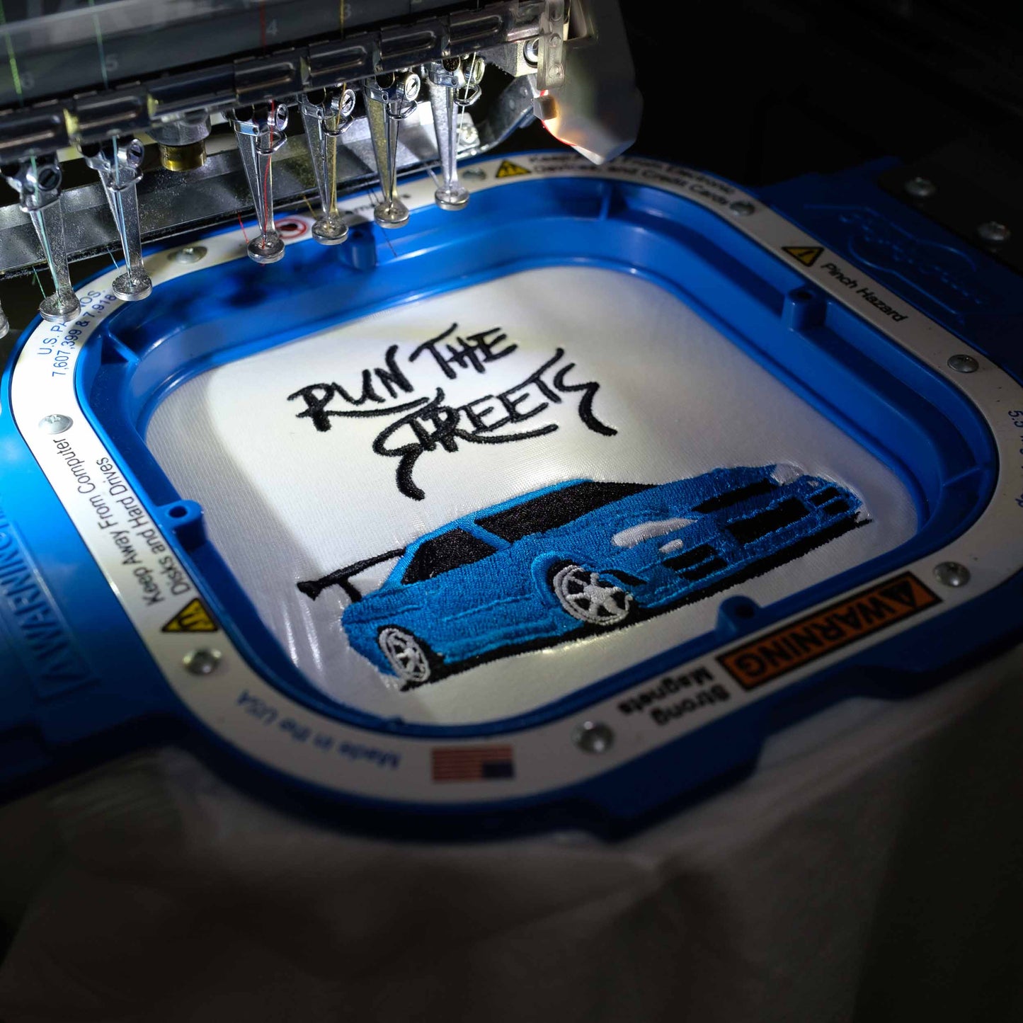 A blue t-shirt with a 4-inch embroidered graphic of a blue Nissan R34 GTR and the phrase 'Run the streets'.