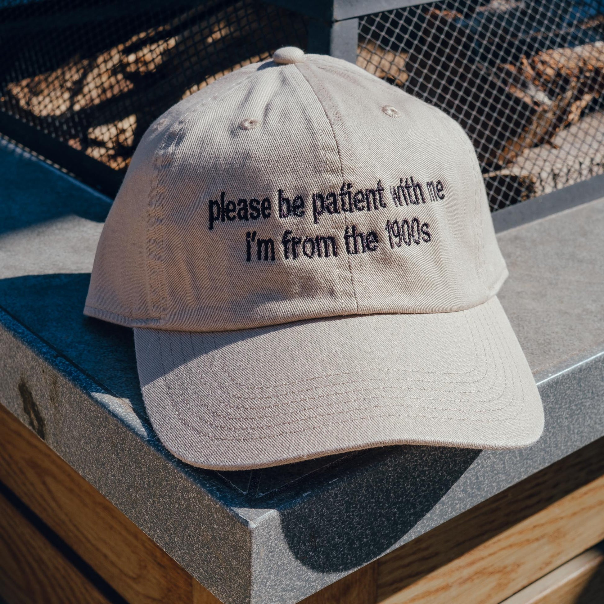 A beige cotton dad hat with the embroidered text 'please be patient with me I'm from the 1900s' in black.