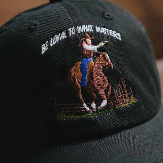 A black embroidered dad hat with a cowboy theme, featuring a quote from a game character.