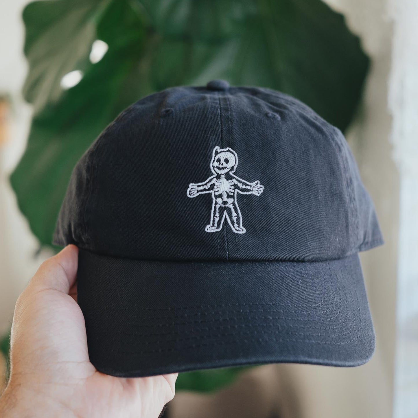 A black dad hat with a glow-in-the-dark embroidered design resembling a character from a popular RPG game.
