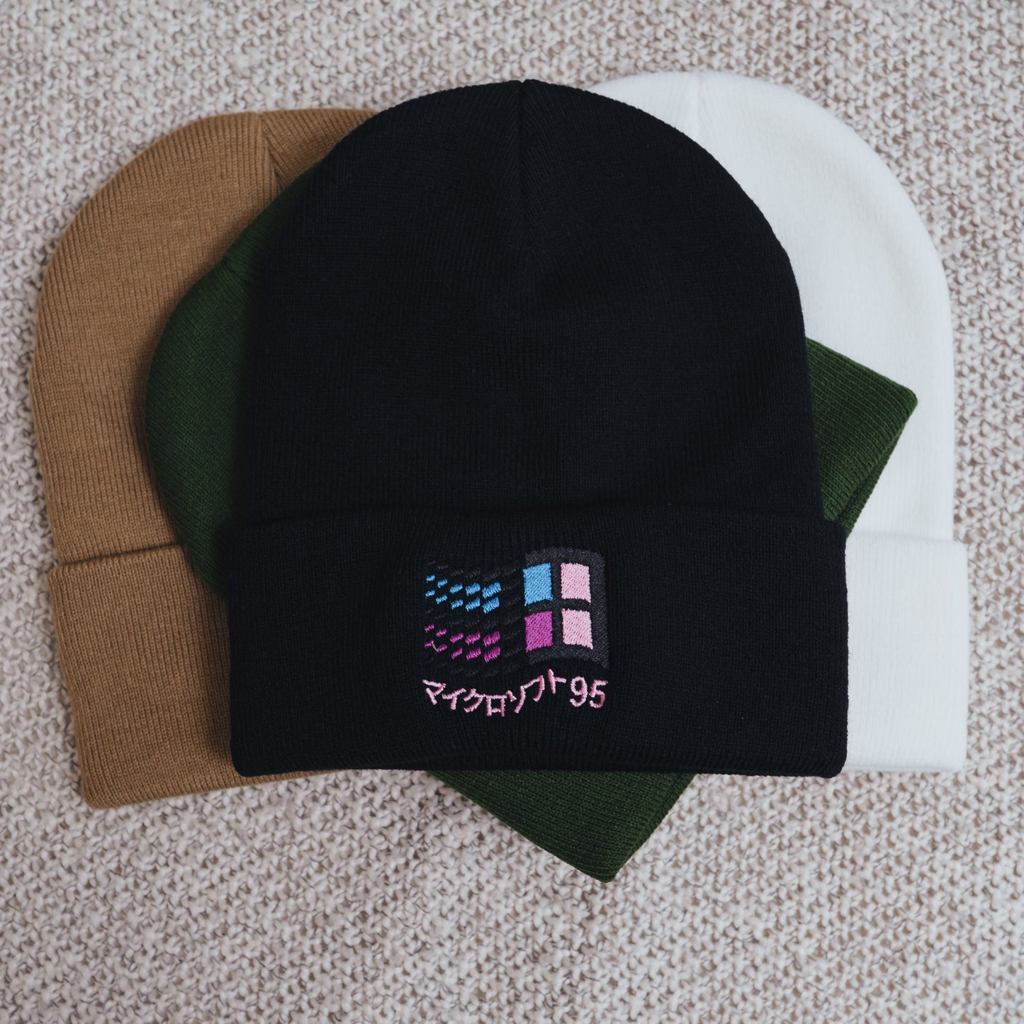A collection of beanies with one featuring an embroidered retro vaporwave design resembling the Windows 95 logo.