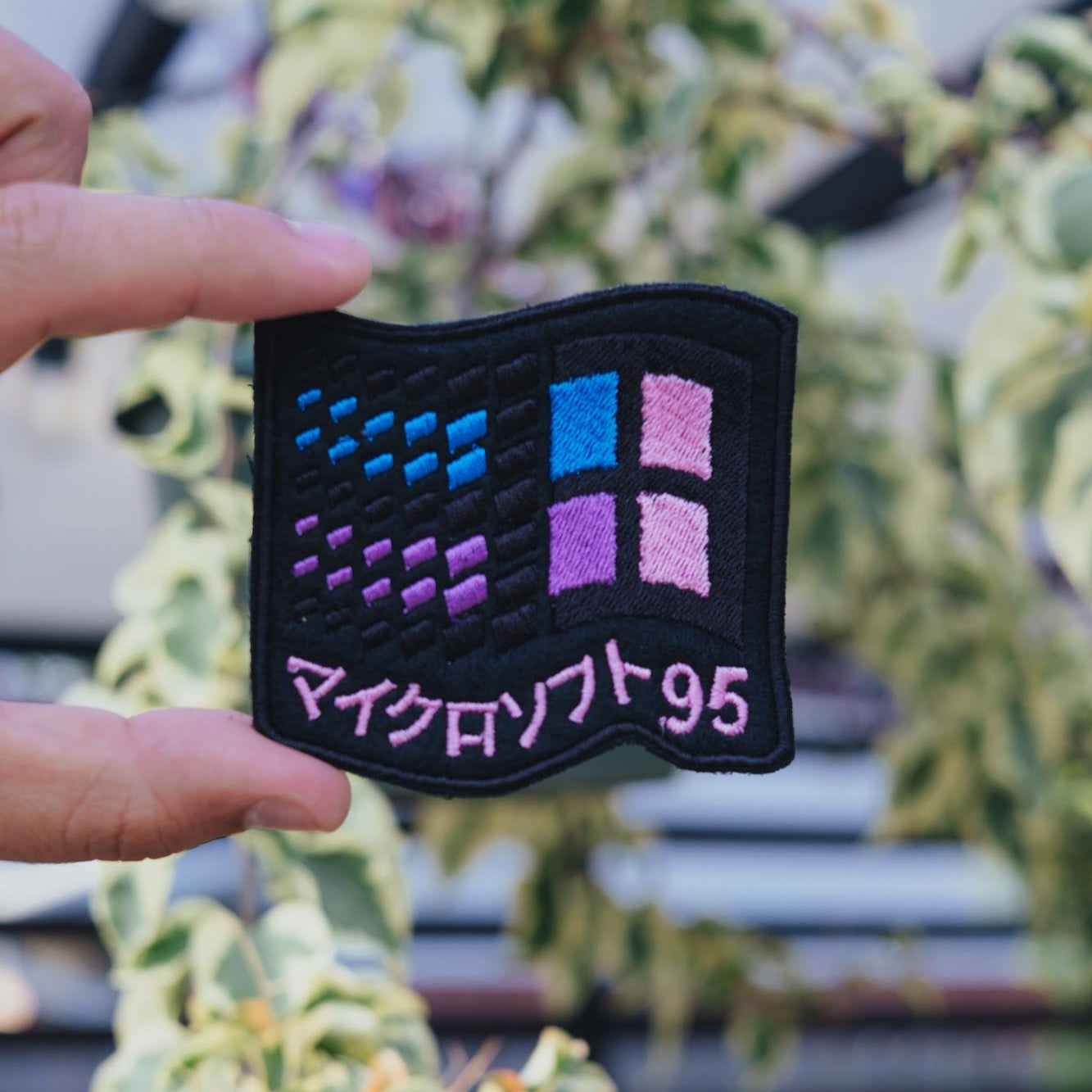 An embroidered patch with a retro vaporwave design, featuring geometric shapes and the text 'Windows 95' in a hand.