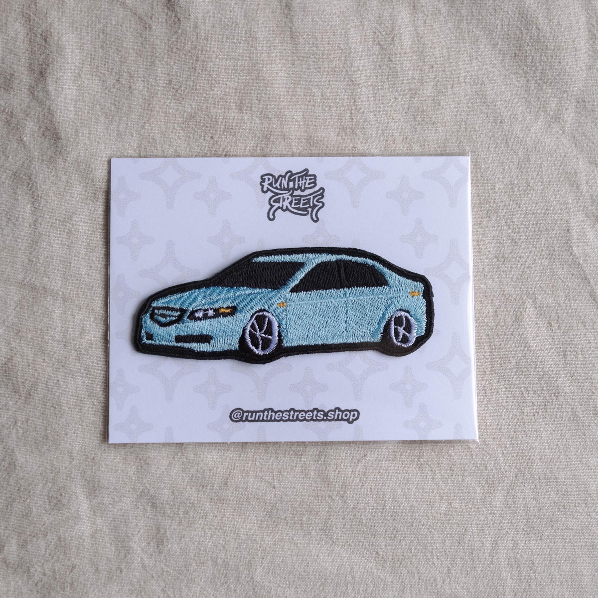 May include: A light blue car patch with black accents, featuring the text "Run the Streets" and "@runthestreets.shop" on a white card with a star pattern. The car has black wheels and a black roof.