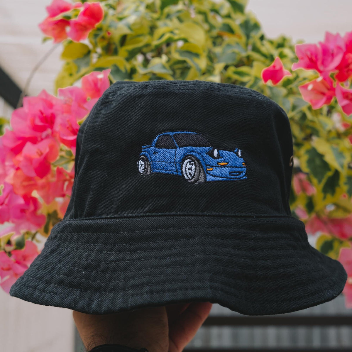 May include: A black bucket hat with a blue car embroidered on the front. The car has headlights and a windshield.