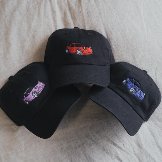 May include: Three black baseball caps with embroidered images of cartoon cars. The cars are red, purple, and blue.